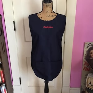 May include: A navy blue sleeveless apron with a single pocket and the text "True Value" embroidered in red on the front.