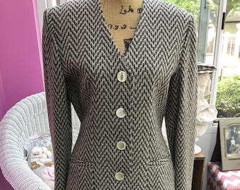 May include: A brown and beige herringbone patterned skirt suit with a V-neck jacket and a skirt that falls to the knee. The jacket has five buttons down the front.