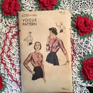 Puede incluir: Patrón de costura Vogue vintage número 6351 para una blusa. El patrón es para la talla 14, 32 de pecho. El patrón muestra tres vistas diferentes de la blusa, una con una tela a cuadros, una con una tela rosa sólida y una con una tela azul sólida.
