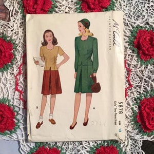 May include: Vintage McCall's sewing pattern for a girl's two-piece dress, size 12. The pattern shows a green dress with a matching hat and a yellow blouse with a brown skirt.