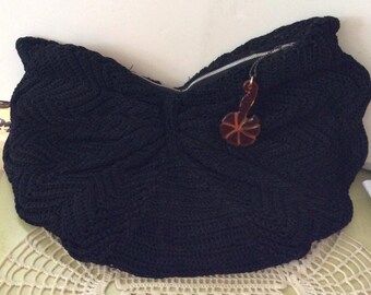 May include: A black crocheted tote bag with a zip closure and a brown plastic decorative charm.