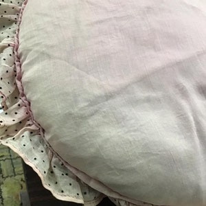 K&ouml;nnte beinhalten: Ein rosa herzf&ouml;rmiges Kissen mit einer wei&szlig;en Spitzenborte und schwarzen Punkten.