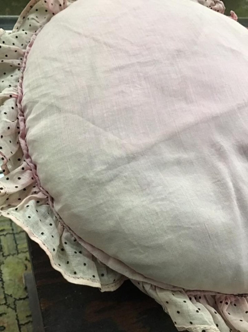K&ouml;nnte beinhalten: Ein rosa herzf&ouml;rmiges Kissen mit einer wei&szlig;en Spitzenborte und schwarzen Punkten.
