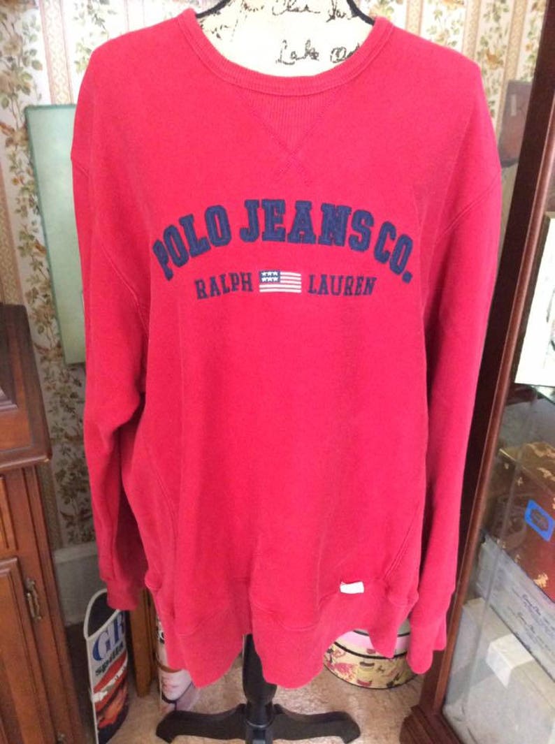 May include: Red long-sleeve sweatshirt with a navy blue embroidered logo that reads "Polo Jeans Co. Ralph Lauren" with a small American flag.