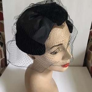 Puede incluir: Un sombrero de terciopelo negro con un gran lazo y un velo de red negro.