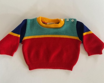 May include: A colorful striped sweater for a baby or toddler. The sweater is red, yellow, blue, and green. It has a round neckline and button closures on the shoulder.