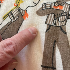 May include: A white cotton t-shirt with a brown and orange illustration of two people. The illustration is in a cartoon style.