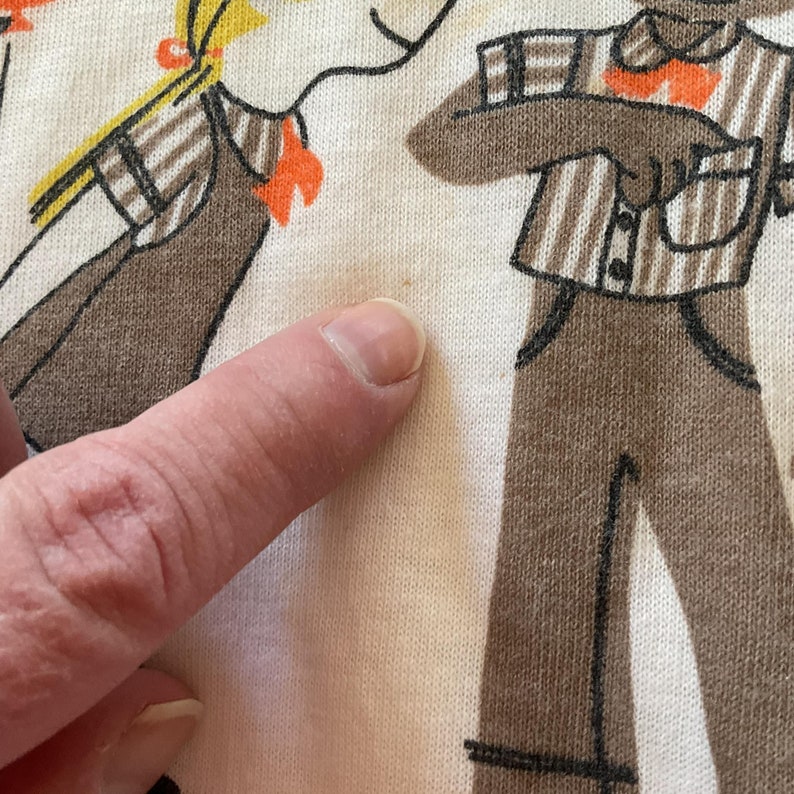 May include: A white cotton t-shirt with a brown and orange illustration of two people. The illustration is in a cartoon style.