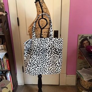 May include: A large black and white leopard print tote bag with black handles. The bag is displayed on a mannequin.