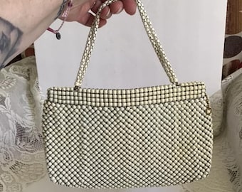 May include: A white beaded purse with a gold chain closure and a short handle. The purse is made of a mesh material and has a vintage look.