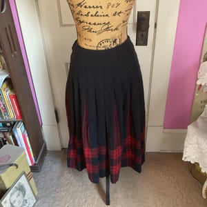May include: A black skirt with a red and black tartan pattern. The skirt is pleated and has a high waist.