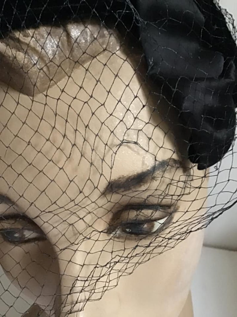 Puede incluir: Un sombrero de terciopelo negro con velo de red negro. El sombrero se lleva en la cabeza de un maniqu&iacute;.