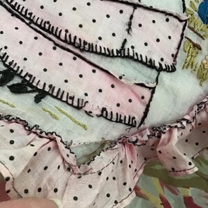 K&ouml;nnte beinhalten: Ein rosa Stoff mit schwarzen Punkten und einem gekr&auml;uselten Rand. Der Stoff ist mit schwarzem Garn gen&auml;ht und hat einen wei&szlig;en Hintergrund.