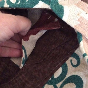 May include: Close-up of a brown fabric with a green and white pattern. The fabric is folded over and the inside is visible. The inside of the fabric is a brown color.