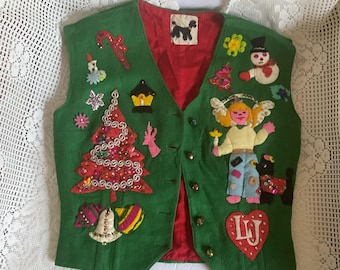 May include: A green felt vest with a red lining and various Christmas-themed appliques, including a Christmas tree, a snowman, a candy cane, and an angel. The vest has a heart-shaped patch with the initials "LJ" on it.