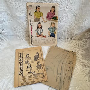 May include: Vintage Simplicity sewing pattern for a blouse with puffed sleeves. The pattern is printed on paper and includes instructions and diagrams. The pattern number is 2001 and the size is 10. The pattern is priced at 25 pence.