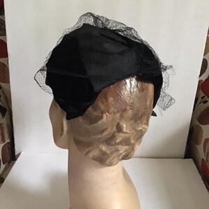 Puede incluir: Un sombrero de terciopelo negro con velo de red negro. El sombrero est&aacute; sentado en una cabeza de maniqu&iacute;.