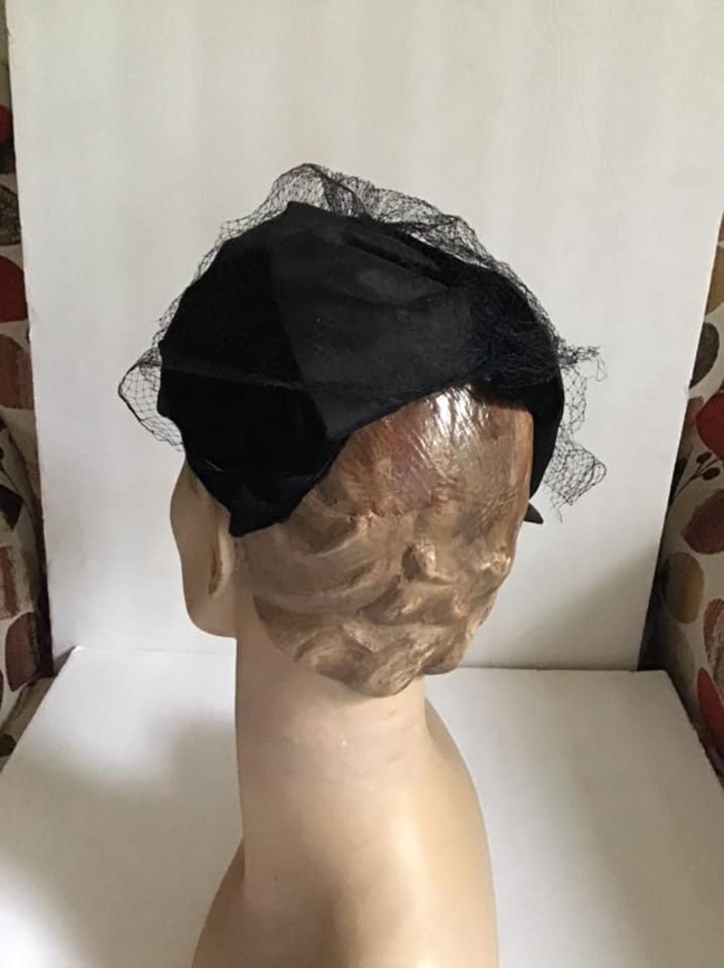 Puede incluir: Un sombrero de terciopelo negro con velo de red negro. El sombrero est&aacute; sentado en una cabeza de maniqu&iacute;.