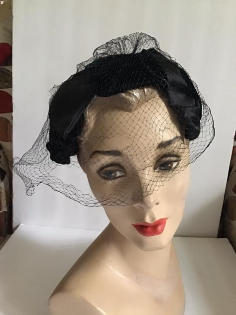 Puede incluir: Una diadema de terciopelo negro con velo de red negro. La diadema se lleva en la cabeza de un maniqu&iacute;.