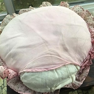 K&ouml;nnte beinhalten: Ein rundes rosa und wei&szlig;es Kissen mit schwarzen Punkten und einem R&uuml;schenrand.