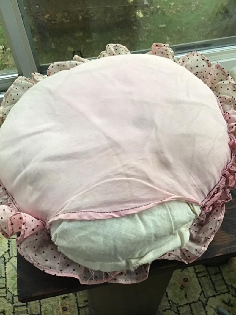 K&ouml;nnte beinhalten: Ein rundes rosa und wei&szlig;es Kissen mit schwarzen Punkten und einem R&uuml;schenrand.