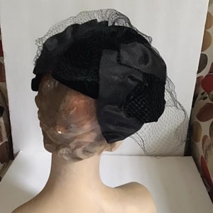 Puede incluir: Un sombrero de terciopelo negro con velo de red negro. El sombrero est&aacute; en una cabeza de maniqu&iacute;.