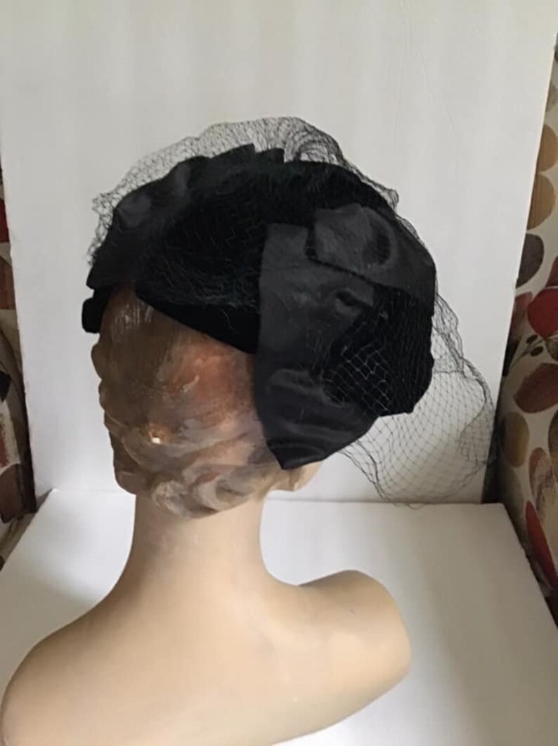 Puede incluir: Un sombrero de terciopelo negro con velo de red negro. El sombrero est&aacute; en una cabeza de maniqu&iacute;.