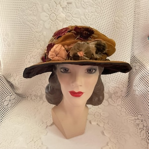 Pode incluir: Um chapéu de veludo castanho com uma aba larga e uma grande flor como adorno. A flor é feita de veludo e tem uma combinação de cores rosa, castanho e verde.