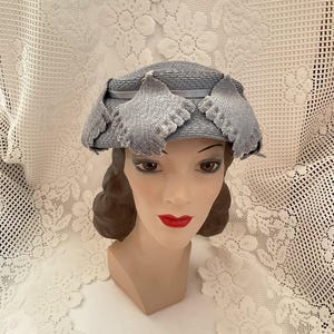 May include: A light blue straw hat with a wide brim and a decorative trim of blue fabric flowers. The hat is on a mannequin head.