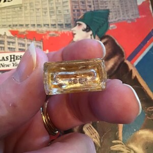 Puede incluir: Una peque&ntilde;a base rectangular de frasco de perfume de vidrio transparente con una marca en relieve en la parte inferior que dice 0689. El vidrio es transparente con un ligero tono &aacute;mbar, mostrando un interior hueco y un borde grueso.