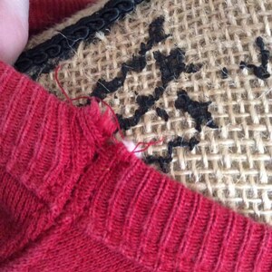 May include: A red knitted sweater with a small tear at the neckline.