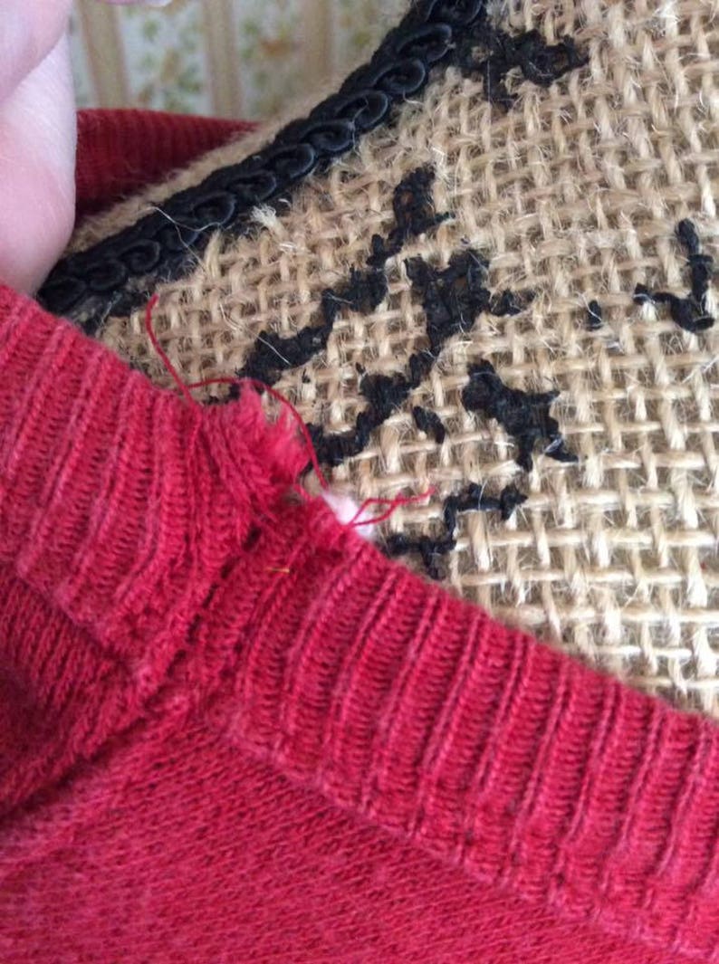 May include: A red knitted sweater with a small tear at the neckline.