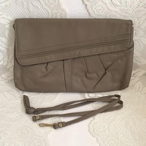 May include: A beige leather clutch with a fold-over flap and a matching strap. The clutch has a textured design and a subtle sheen.
