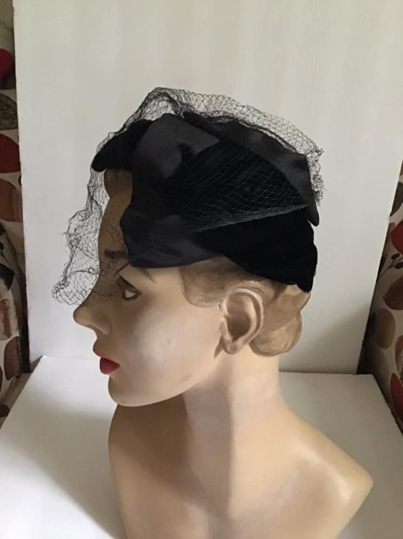 Puede incluir: Un sombrero de terciopelo negro con velo de red negro. El sombrero se lleva en la cabeza de un maniqu&iacute;.