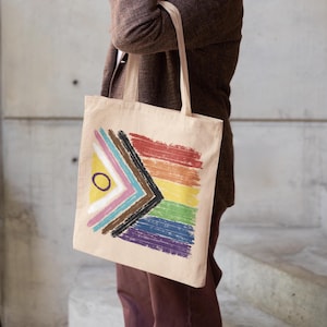 Könnte beinhalten: Beige Tragetasche mit einem farbenfrohen, abstrakten Design. Das Design beinhaltet einen Regenbogen aus Farben und eine geometrische Form mit einem gelben Kreis. Die Tasche hat lange Henkel und ist aus einem robusten Stoff gefertigt.