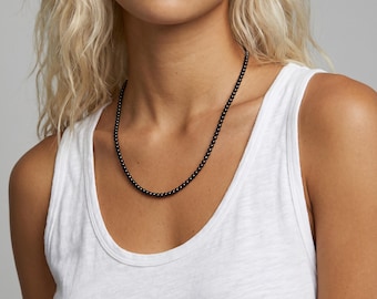 Puede incluir: Un collar compuesto por pequeñas cuentas esféricas negras, uniformes y brillantes, ensartadas en una sola hebra. Las cuentas tienen una superficie lisa y reflectante, dispuestas en un patrón circular continuo alrededor del cuello.