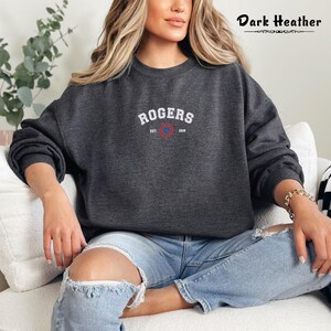 Może przedstawiać: Szara bluza w kolorze ciemnego melanżu z haftowanym białym logo z napisem "ROGERS EST. 1903" i czerwono-niebieskim k&oacute;łkiem.