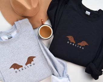 May include: Two sweatshirts with a bat wing graphic and the word "Darling" printed on them. One sweatshirt is gray and the other is black.