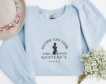 May include: Light blue sweatshirt with the text "Anyone can cook" in a circle around a silhouette of a rat holding a cooking utensil. The text "Paris - France" is below the rat and the text "Gusteau's" is below that. Five stars are below the text "Gusteau's".