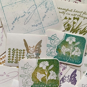 May include: A collection of handmade cards with various designs and text. Some cards feature floral illustrations and the phrase "Consider the Lily." Other cards have phrases like "It is never too late to be what you might have been."