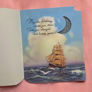 May include: Vintage birthday card featuring a sailing ship on a wavy sea under a blue sky with clouds. The card has a crescent moon cutout with glitter and the text: "May the Birthday course you steer Take you straight to a happy year;"