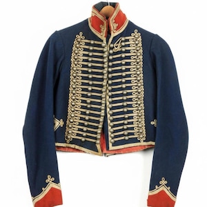 May include: A vintage navy blue military jacket with gold trim and buttons. The jacket features a red collar and cuffs, and is adorned with decorative gold embroidery. The jacket is displayed on a wooden hanger.