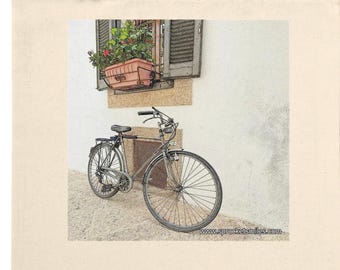 May include: A cream-coloured tote bag displaying a vintage bicycle parked by a window with a flower box. The image has a soft, artistic style, suggesting European charm. The bag has long handles.