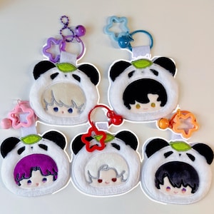 Pode incluir: Uma coleção de seis chaveiros com tema de panda em branco, preto e verde. Cada chaveiro apresenta um rosto de panda com o rosto de um personagem dentro. Os chaveiros têm acessórios em forma de estrela de várias cores e pequenos sinos.