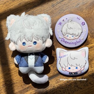 May include: A plush cat doll with a blue and white outfit, a white tail, and a keychain. Also included are two cat-themed badges, one round and one cat-shaped, with the text "Shenxinghui" and "meow~".