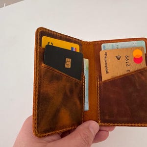 May include: Open brown leather wallet with multiple card slots, filled with various credit cards and identification cards. The wallet has a worn, textured appearance and is held open, showcasing its contents.