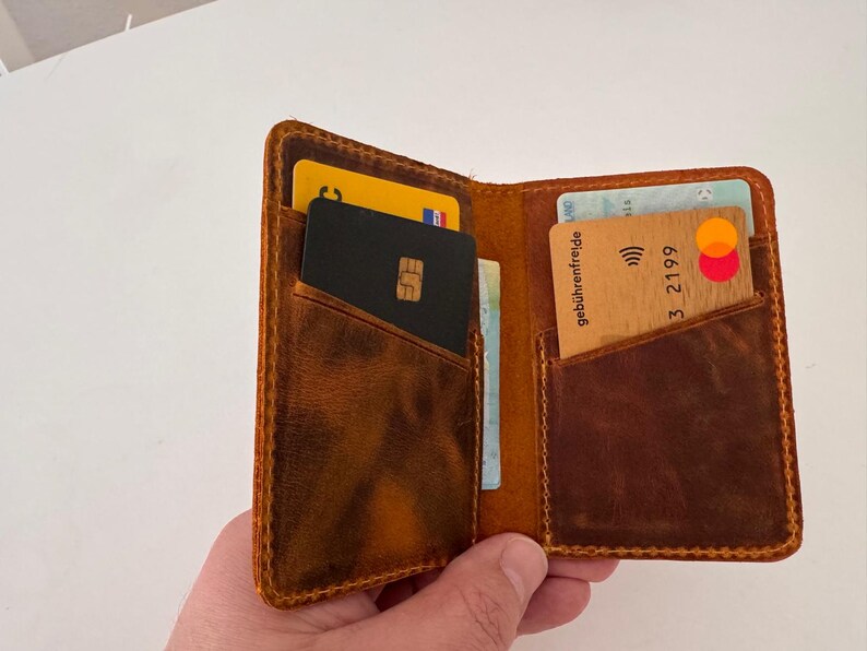 May include: Open brown leather wallet with multiple card slots, filled with various credit cards and identification cards. The wallet has a worn, textured appearance and is held open, showcasing its contents.
