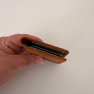 May include: A small, open, brown leather card holder, held in a hand. The wallet is filled with several cards. The leather has a slightly distressed appearance. The wallet is approximately 4 inches long.
