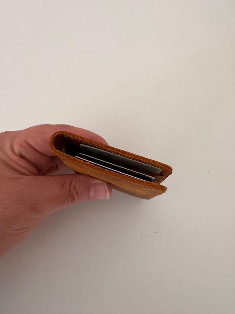 May include: A small, open, brown leather card holder, held in a hand. The wallet is filled with several cards. The leather has a slightly distressed appearance. The wallet is approximately 4 inches long.