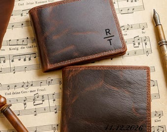 May include: Two brown leather wallets with personalized initials and date stamps. The wallets are rectangular with a distressed finish, set on a vintage sheet music background. One wallet has "R/T" and the other has "11.12.2026" engraved.
